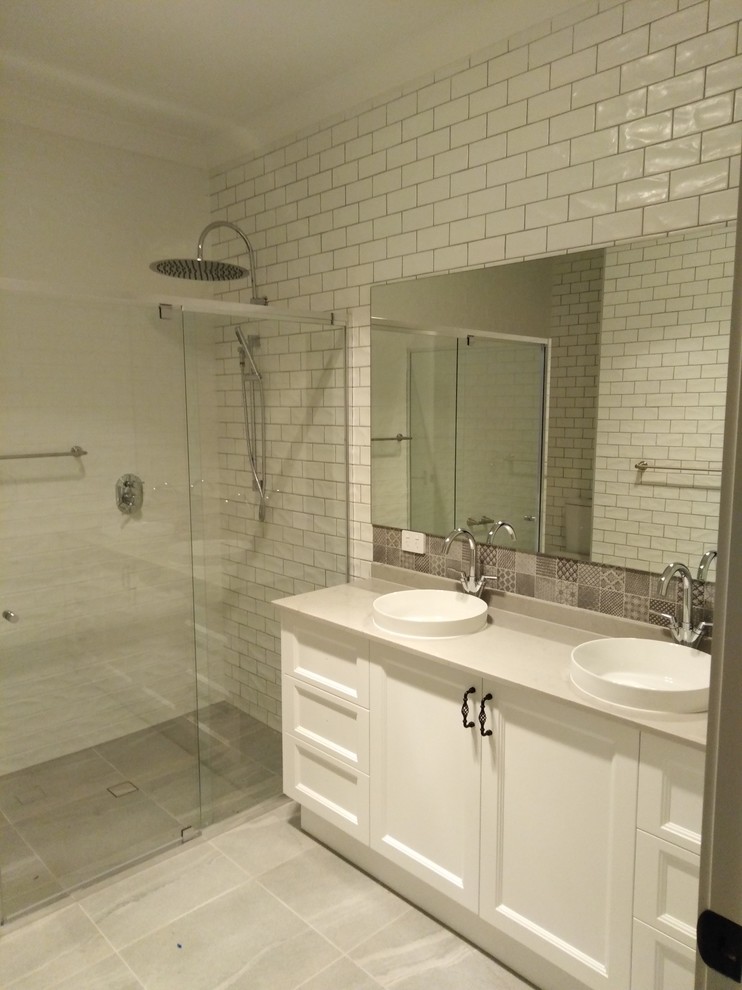 Inspiration for a mid-sized contemporary master bathroom in Brisbane with raised-panel cabinets, white cabinets, a double shower, a one-piece toilet, white tile, ceramic tile, white walls, ceramic floors, a console sink, limestone benchtops, grey floor, a hinged shower door and white benchtops.