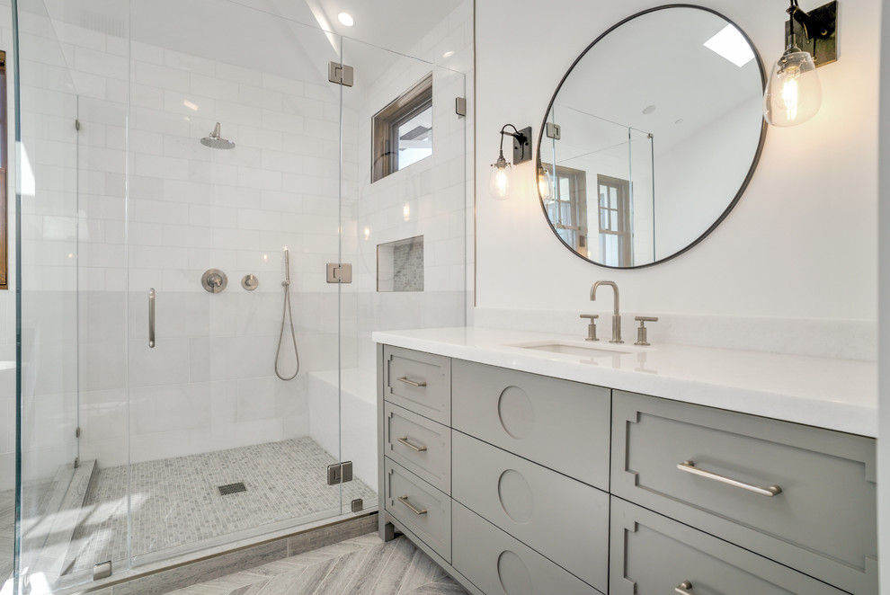 This is an example of a transitional 3/4 bathroom in Los Angeles with grey cabinets, a corner shower, white tile, white walls, an undermount sink, grey floor, a hinged shower door and recessed-panel cabinets.