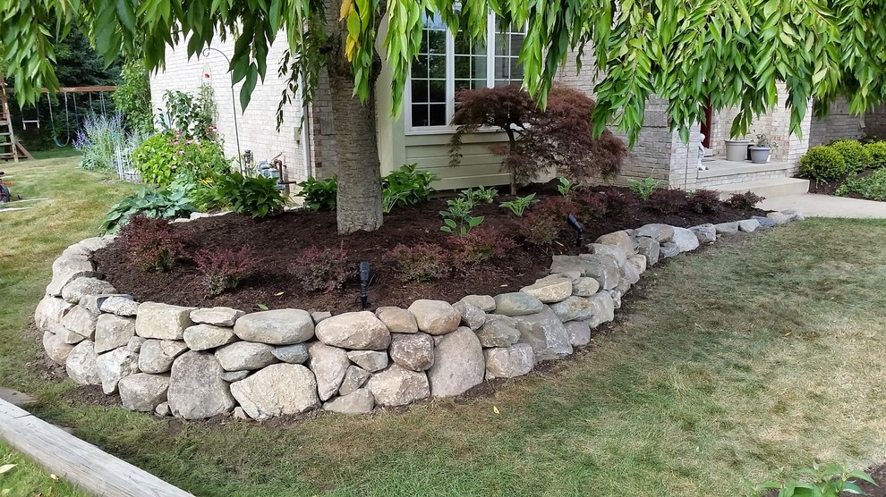 This is an example of a mid-sized traditional front yard partial sun garden for summer in Detroit with a retaining wall and mulch.