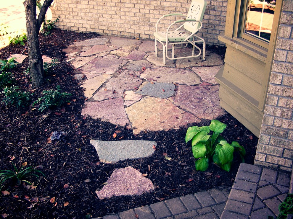 This is an example of a small traditional side yard patio in Minneapolis with natural stone pavers and a roof extension.
