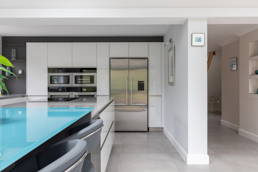 This is an example of a large contemporary open plan kitchen in Sussex with flat-panel cabinets, white cabinets, composite countertops, grey splashback, an island and grey worktops.