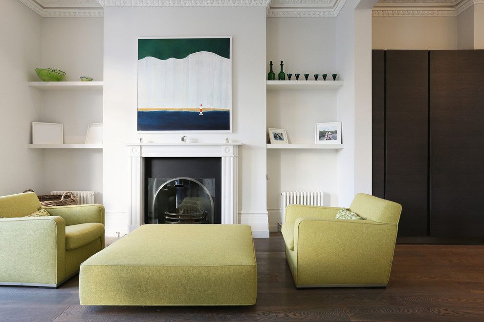 This is an example of a mid-sized contemporary open concept living room in London with a library, white walls, medium hardwood floors, a standard fireplace, a plaster fireplace surround and no tv.