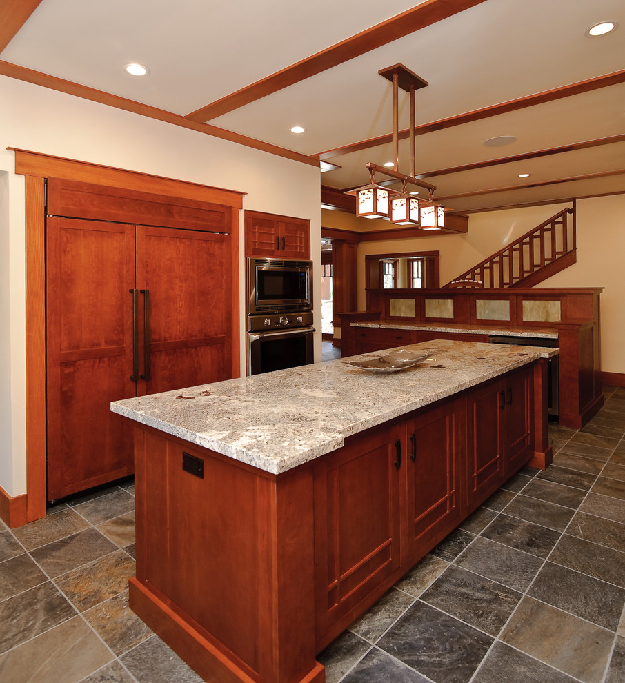 This is an example of a large arts and crafts l-shaped kitchen pantry in Orange County with an undermount sink, shaker cabinets, dark wood cabinets, marble benchtops, beige splashback, stone slab splashback, stainless steel appliances, travertine floors and with island.