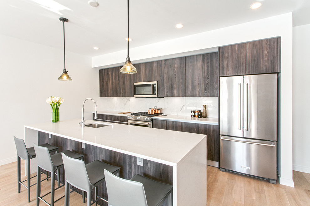 This is an example of a mid-sized contemporary single-wall kitchen in New York with an undermount sink, flat-panel cabinets, dark wood cabinets, white splashback, stainless steel appliances, light hardwood floors, beige floor and with island.