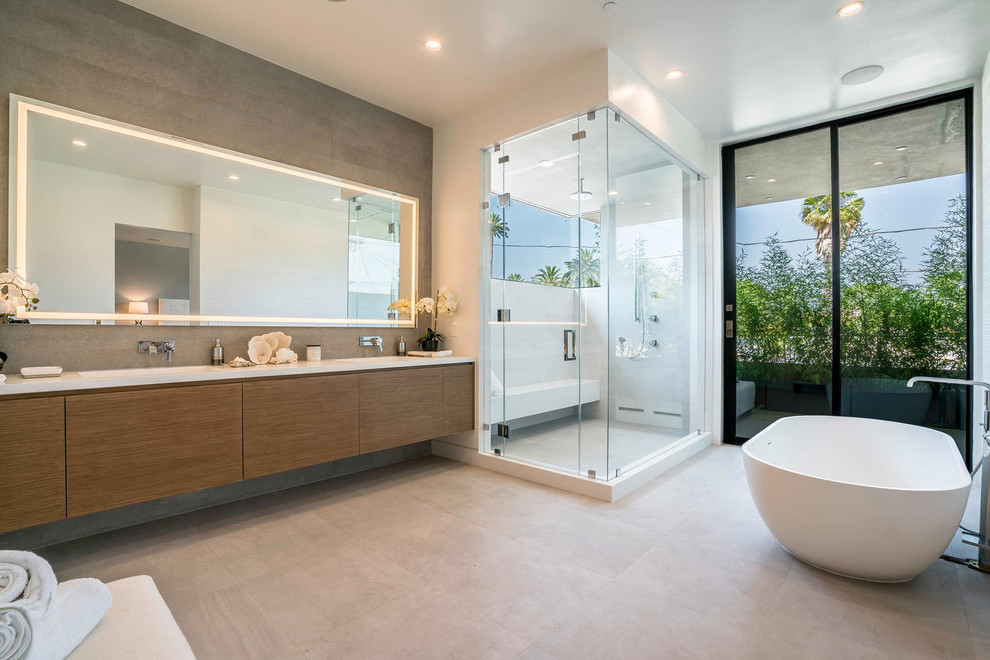 Photo of a contemporary master bathroom in Los Angeles with flat-panel cabinets, medium wood cabinets, a freestanding tub, a corner shower, gray tile, white tile, white walls, beige floor and a hinged shower door.