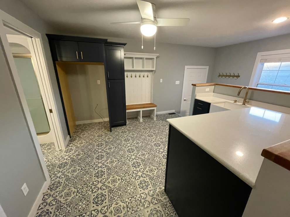 Example of a country vinyl floor and multicolored floor laundry room design in St Louis with a farmhouse sink, shaker cabinets, blue cabinets, quartz countertops, white backsplash, quartz backsplash, blue walls, a concealed washer/dryer and white countertops