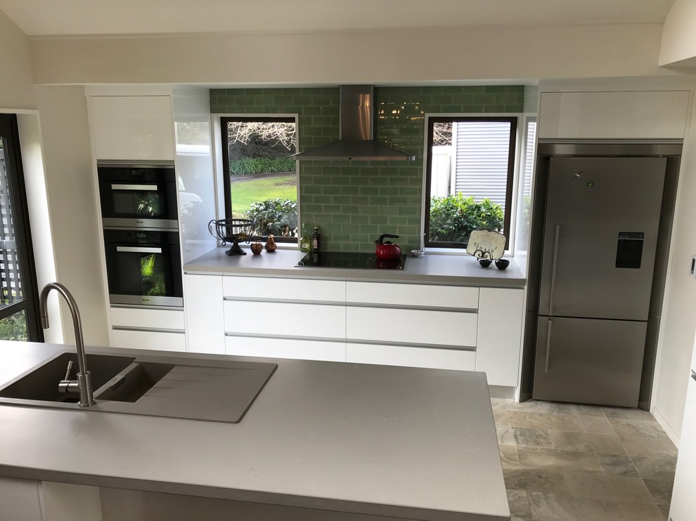 Design ideas for a large contemporary galley open plan kitchen in Christchurch with a double-bowl sink, white cabinets, quartz benchtops, green splashback, glass tile splashback, stainless steel appliances, porcelain floors, a peninsula and multi-coloured floor.