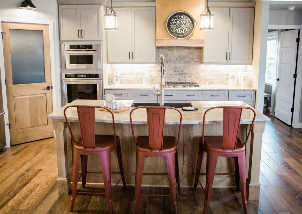 Example of a mid-sized transitional kitchen design with a farmhouse sink, granite countertops, gray backsplash, stainless steel appliances and an island