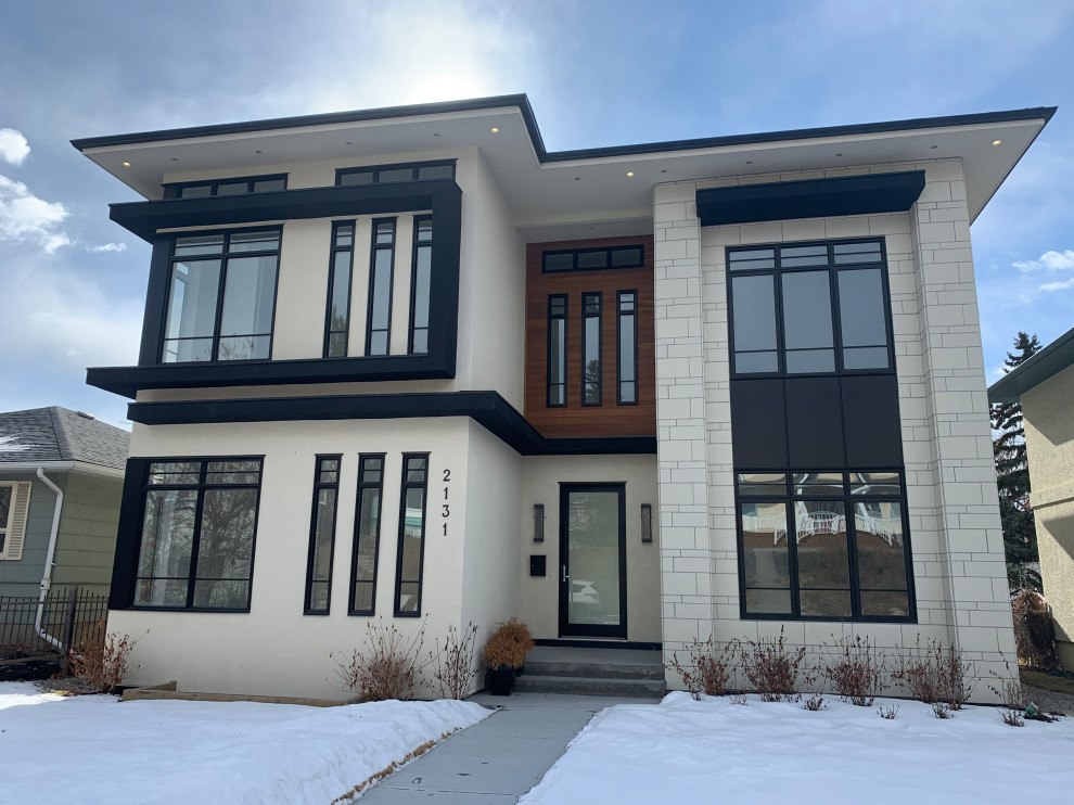 This is an example of a mid-sized contemporary two-storey white house exterior in Calgary with stone veneer and a flat roof.
