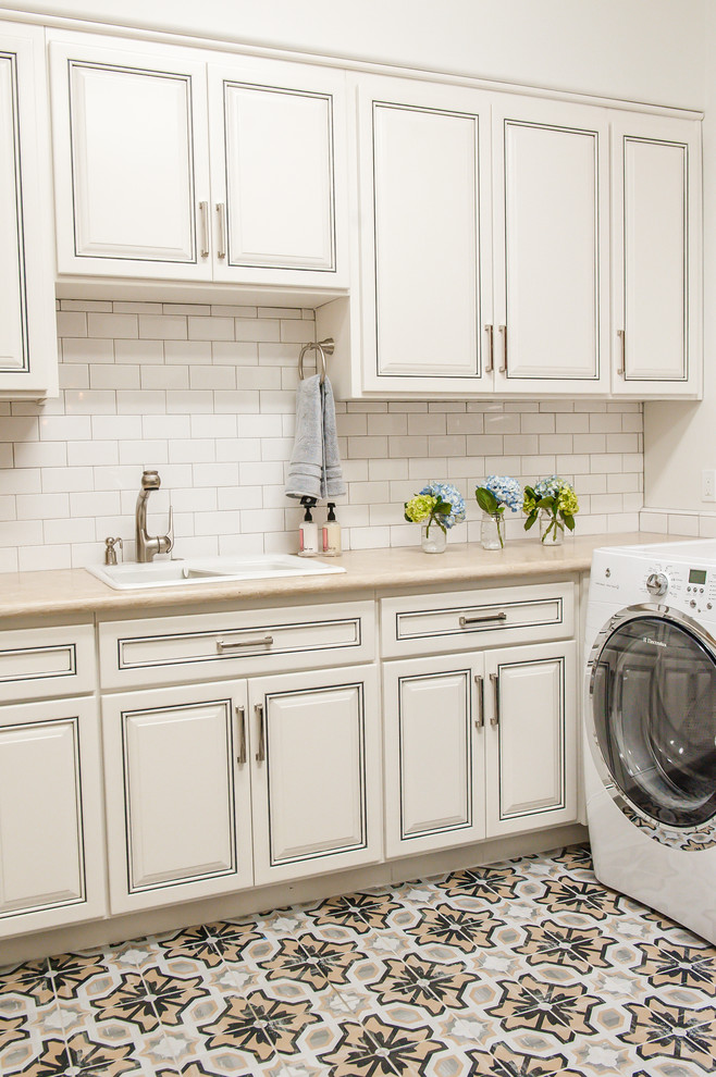 Photo of a large transitional l-shaped laundry cupboard in Phoenix with an undermount sink, raised-panel cabinets, white cabinets, solid surface benchtops, white walls, terra-cotta floors and a side-by-side washer and dryer.