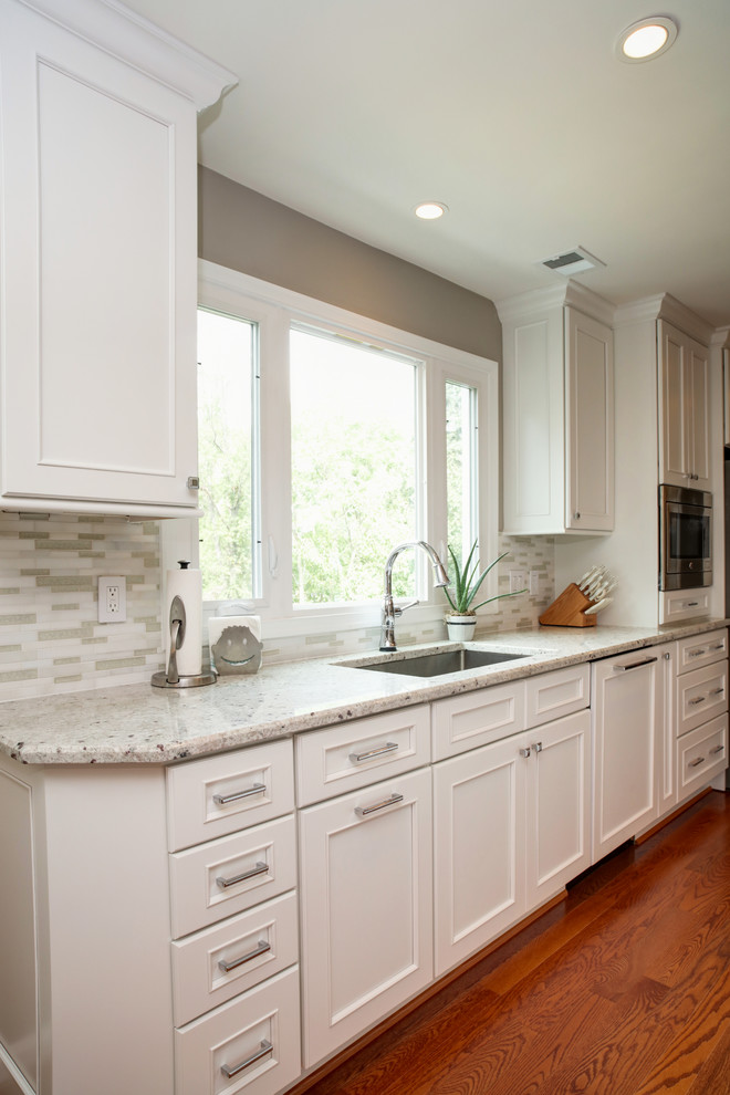 Mid-sized transitional u-shaped medium tone wood floor eat-in kitchen photo in DC Metro with a single-bowl sink, beaded inset cabinets, white cabinets, quartz countertops, white backsplash, matchstick tile backsplash, stainless steel appliances and an island