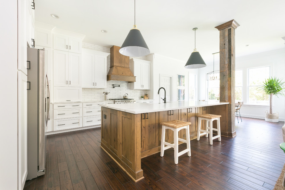 This is an example of an expansive country open plan kitchen in Charleston with a farmhouse sink, shaker cabinets, white cabinets, quartz benchtops, white splashback, brick splashback, stainless steel appliances, with island and white benchtop.