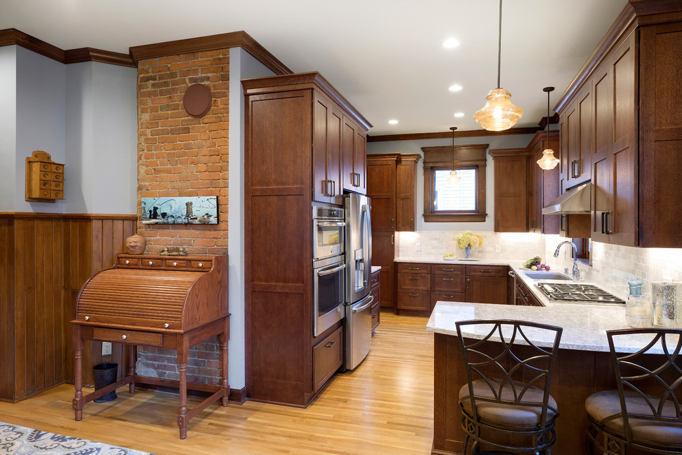 Photo of a large arts and crafts u-shaped eat-in kitchen in Minneapolis with an undermount sink, medium wood cabinets, quartz benchtops, marble splashback, stainless steel appliances, light hardwood floors, a peninsula, yellow floor, shaker cabinets and white splashback.