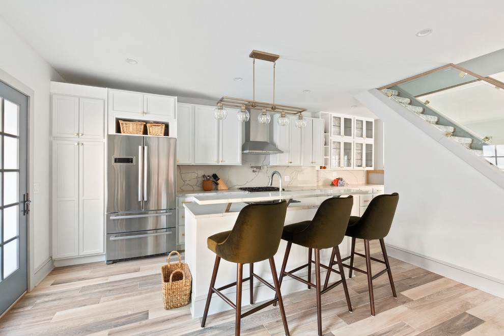 This is an example of a mid-sized transitional single-wall eat-in kitchen in New York with shaker cabinets, white cabinets, with island, marble benchtops, grey splashback, stone slab splashback, stainless steel appliances, light hardwood floors and brown floor.