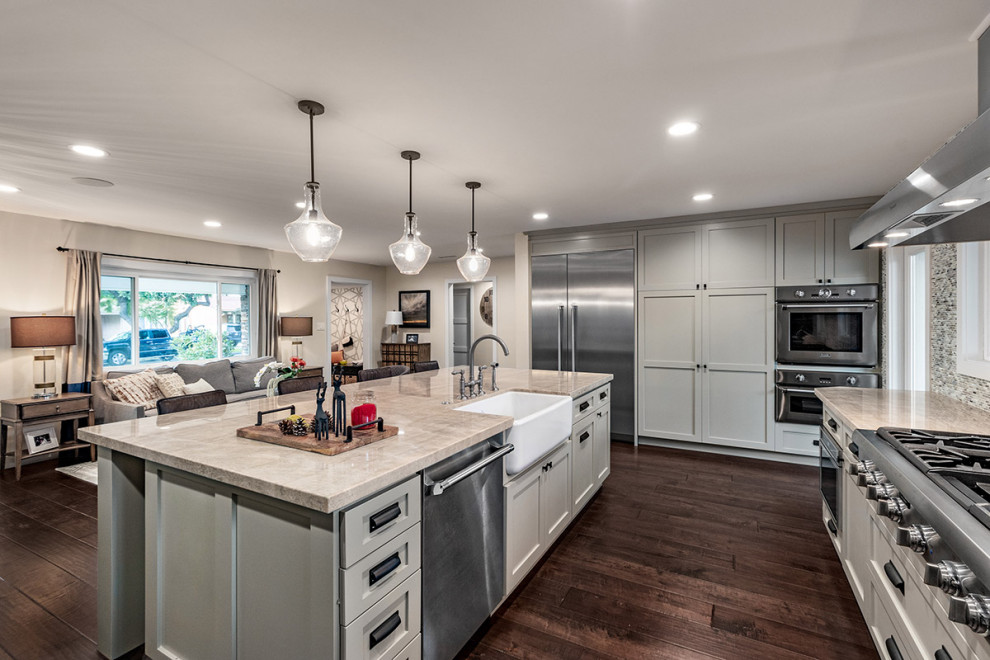 Inspiration for a large transitional galley eat-in kitchen in Los Angeles with a farmhouse sink, shaker cabinets, quartzite benchtops, beige splashback, mosaic tile splashback, stainless steel appliances, dark hardwood floors, with island, brown floor, grey benchtop and beige cabinets.