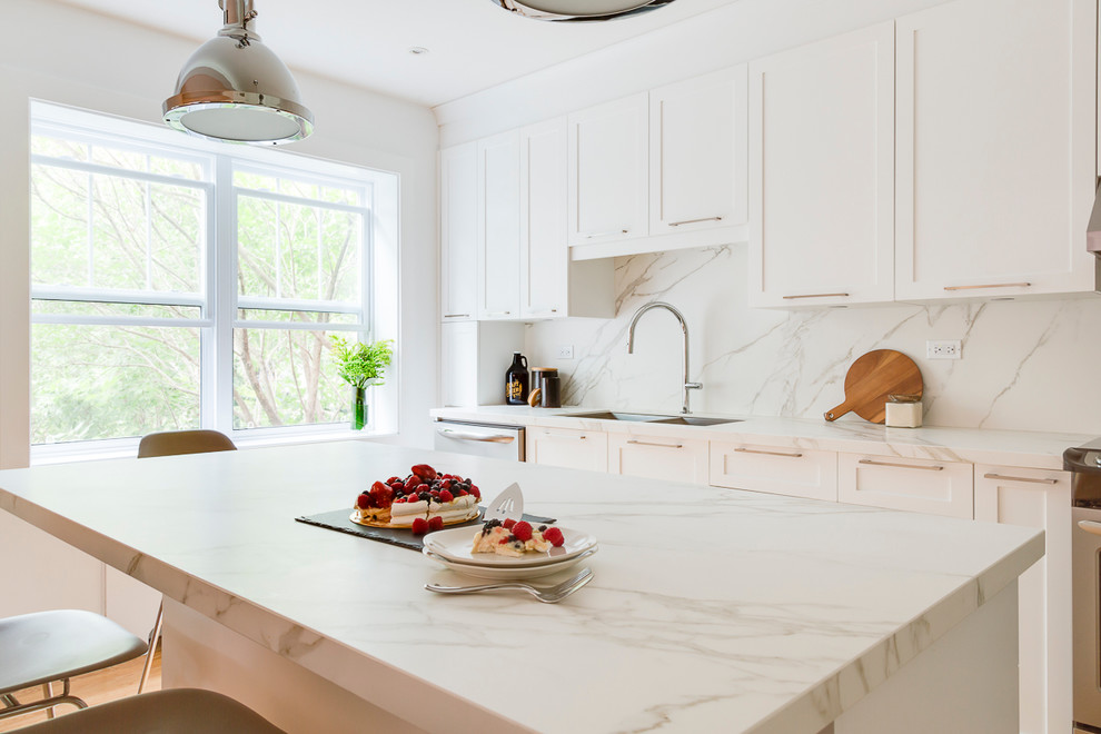 Design ideas for a mid-sized transitional l-shaped eat-in kitchen in Montreal with a double-bowl sink, shaker cabinets, white cabinets, marble benchtops, white splashback, stone slab splashback, light hardwood floors, with island and stainless steel appliances.