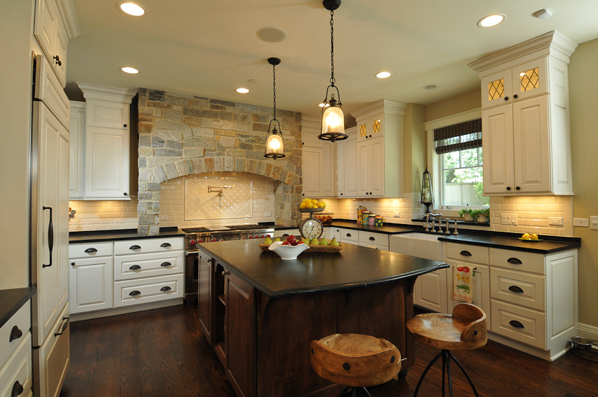 Example of a mountain style l-shaped eat-in kitchen design in Chicago with a farmhouse sink, raised-panel cabinets, white cabinets, soapstone countertops, white backsplash, subway tile backsplash and paneled appliances