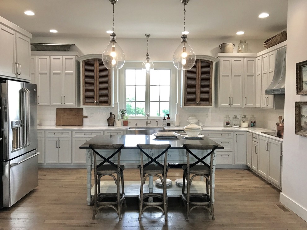 Inspiration for a large timeless u-shaped light wood floor and brown floor eat-in kitchen remodel with a farmhouse sink, flat-panel cabinets, gray cabinets, marble countertops, white backsplash, ceramic backsplash, stainless steel appliances and an island
