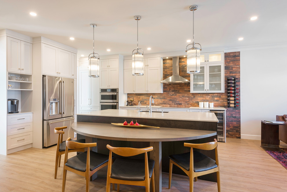 Photo of a mid-sized transitional eat-in kitchen in Vancouver with a farmhouse sink, shaker cabinets, white cabinets, quartz benchtops, brown splashback, brick splashback, stainless steel appliances, vinyl floors, with island, beige floor and beige benchtop.
