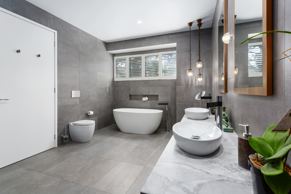 Design ideas for a mid-sized contemporary 3/4 bathroom in Melbourne with flat-panel cabinets, medium wood cabinets, a curbless shower, a two-piece toilet, white tile, white walls, concrete floors, a wall-mount sink, granite benchtops, grey floor, a hinged shower door, white benchtops, a freestanding tub and ceramic tile.