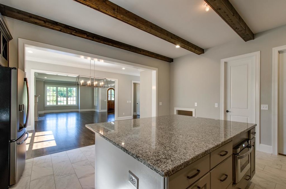 Example of a mid-sized transitional l-shaped ceramic tile and white floor open concept kitchen design with an undermount sink, raised-panel cabinets, brown cabinets, granite countertops, white backsplash, ceramic backsplash, stainless steel appliances and an island