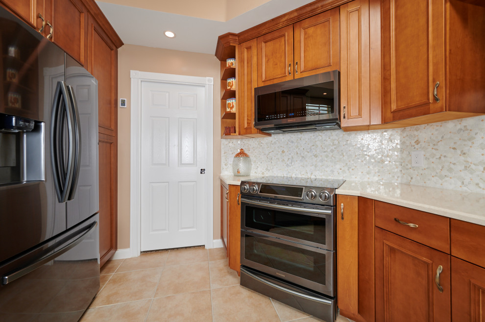 Example of a mid-sized transitional galley porcelain tile, beige floor and tray ceiling kitchen design with a farmhouse sink, recessed-panel cabinets, medium tone wood cabinets, quartz countertops, multicolored backsplash, marble backsplash, stainless steel appliances, a peninsula and beige countertops