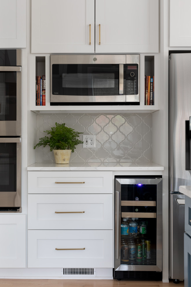 Eat-in kitchen - mid-sized transitional light wood floor and brown floor eat-in kitchen idea with shaker cabinets, gray backsplash, stainless steel appliances, an island and white countertops