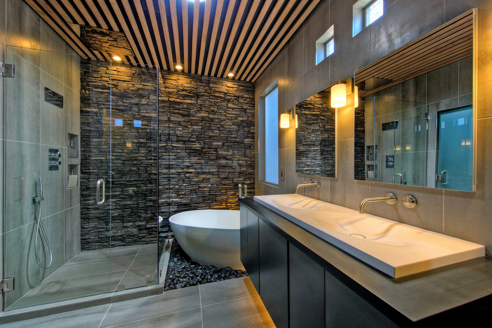 Mid-sized contemporary master bathroom in Phoenix with flat-panel cabinets, dark wood cabinets, a freestanding tub, a corner shower, a one-piece toilet, gray tile, porcelain tile, grey walls, porcelain floors, a wall-mount sink and solid surface benchtops.