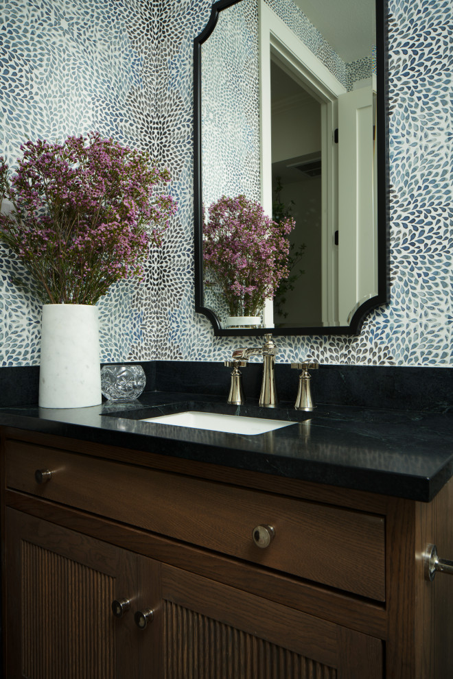 This is an example of a medium sized traditional cloakroom in Austin with beaded cabinets, medium wood cabinets, a one-piece toilet, white tiles, porcelain tiles, limestone flooring, a submerged sink, soapstone worktops, grey floors, black worktops, a built in vanity unit and wallpapered walls.