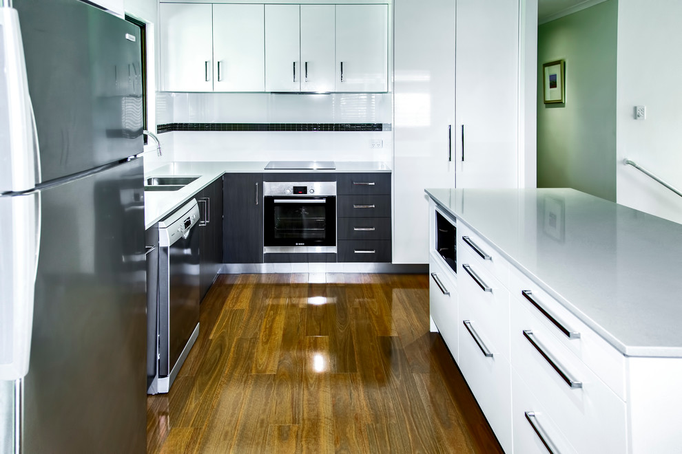 Design ideas for a mid-sized modern l-shaped eat-in kitchen in Sunshine Coast with an undermount sink, flat-panel cabinets, white cabinets, quartz benchtops, white splashback, ceramic splashback, stainless steel appliances, medium hardwood floors and with island.