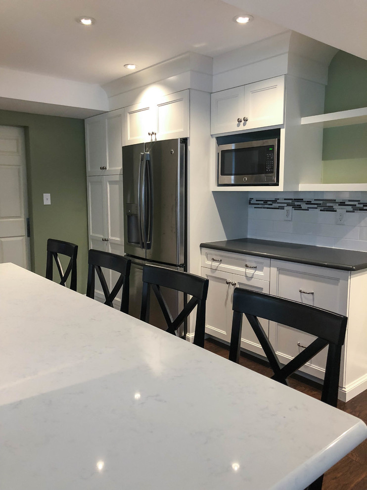 This is an example of a large transitional l-shaped eat-in kitchen in Philadelphia with a drop-in sink, shaker cabinets, white cabinets, multi-coloured splashback, ceramic splashback, stainless steel appliances, dark hardwood floors, with island, brown floor, white benchtop and coffered.