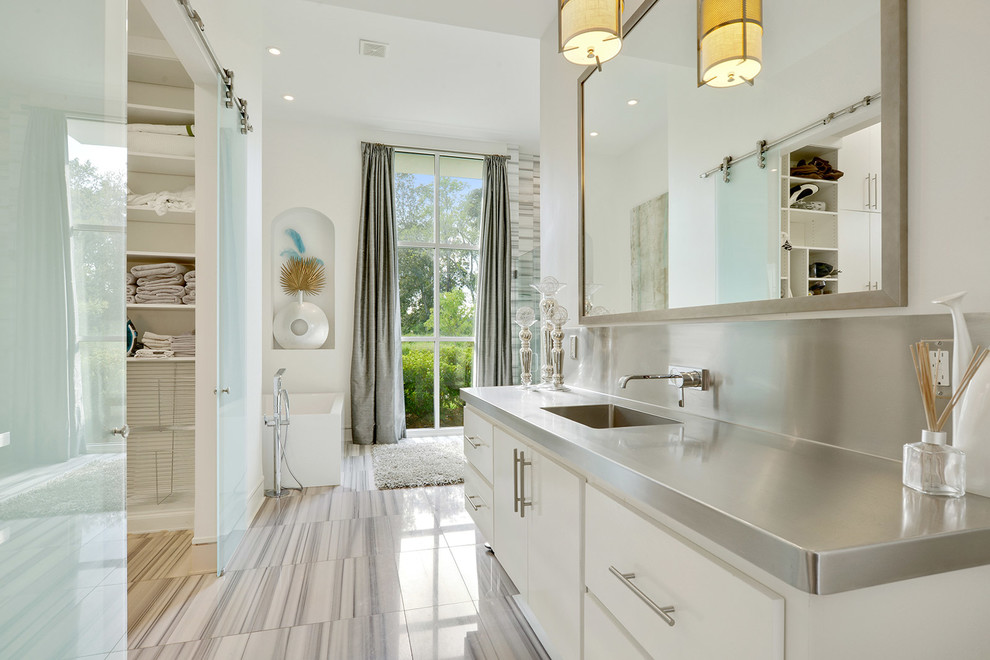 Inspiration for a modern master bathroom in New Orleans with flat-panel cabinets, white cabinets, a freestanding tub, a corner shower, gray tile, stone tile, white walls, marble floors, an integrated sink, stainless steel benchtops, grey floor and a hinged shower door.