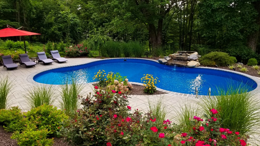 Inspiration for a mid-sized traditional backyard custom-shaped pool in New York with a water feature and concrete pavers.