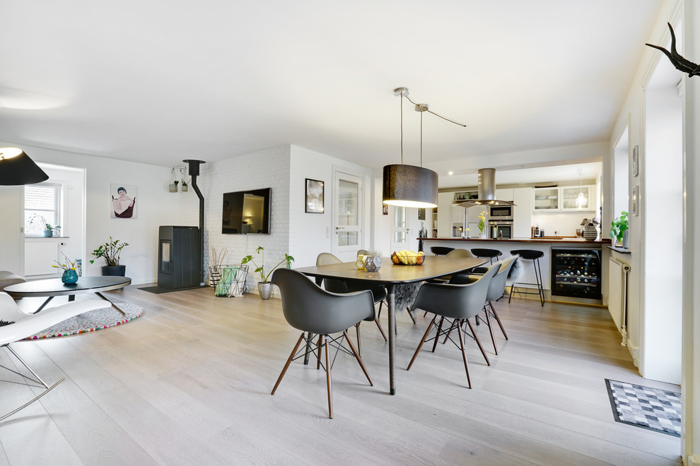 Mid-sized scandinavian open plan dining in Copenhagen with white walls, light hardwood floors, a wood stove, a metal fireplace surround and beige floor.