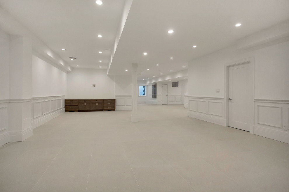 Aménagement d'un très grand sous-sol moderne donnant sur l'extérieur avec un mur blanc, un sol en carrelage de porcelaine et un sol beige.