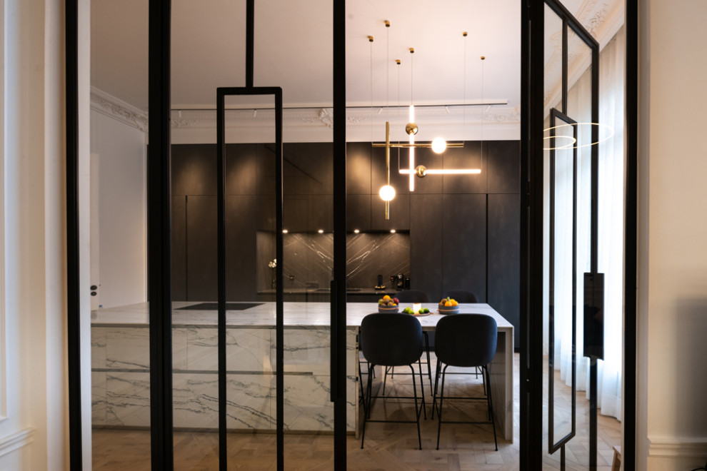 This is an example of a large contemporary single-wall separate kitchen in Paris with an undermount sink, beaded inset cabinets, black cabinets, marble benchtops, black splashback, marble splashback, panelled appliances, light hardwood floors, with island, beige floor and white benchtop.