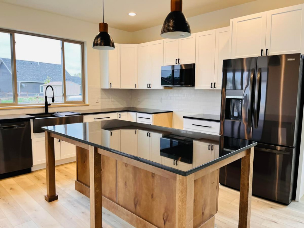 Idée de décoration pour une cuisine champêtre en L et bois clair avec un évier de ferme, un placard à porte shaker, un plan de travail en quartz modifié, une crédence blanche, une crédence en carrelage métro, un électroménager noir, sol en stratifié, îlot et plan de travail noir.