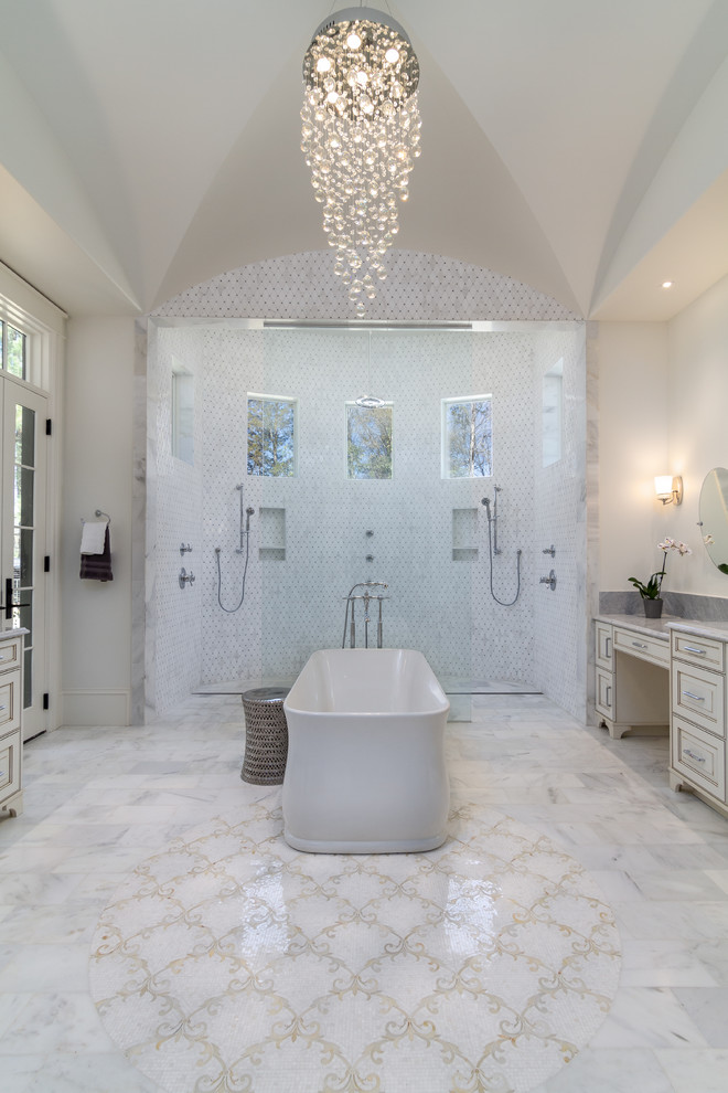 This is an example of a large mediterranean master bathroom in Charlotte with raised-panel cabinets, white cabinets, a freestanding tub, a shower/bathtub combo, a two-piece toilet, white tile, porcelain tile, white walls, marble floors, an undermount sink, granite benchtops, multi-coloured floor, an open shower and grey benchtops.