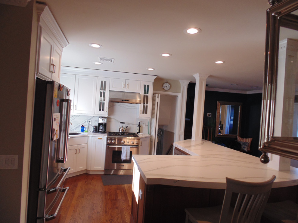 Inspiration for a mid-sized transitional u-shaped medium tone wood floor and brown floor eat-in kitchen remodel with an undermount sink, recessed-panel cabinets, white cabinets, quartz countertops, white backsplash, stone slab backsplash, stainless steel appliances, no island and white countertops