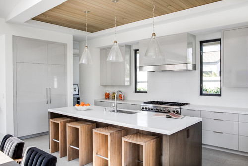 Modern kitchen with white slab cabinets, waterfall island, wood stools, integrated fridge, and glass pendant lights