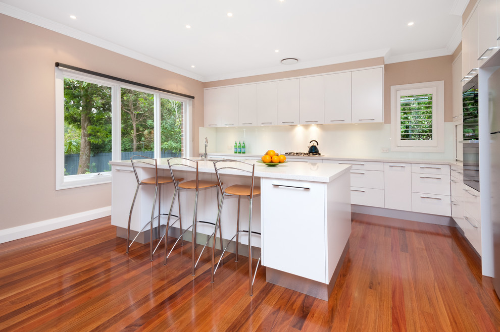 Inspiration for a large contemporary l-shaped open plan kitchen in Sydney with a double-bowl sink, flat-panel cabinets, white cabinets, glass sheet splashback, stainless steel appliances, medium hardwood floors and with island.