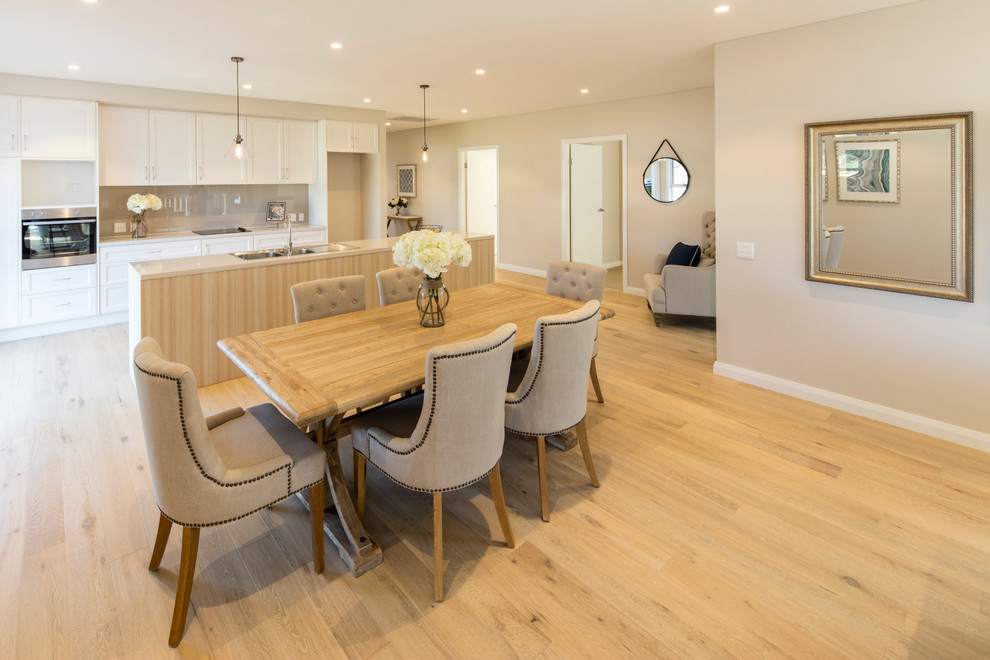 Large contemporary single-wall open plan kitchen in Sydney with a double-bowl sink, shaker cabinets, white cabinets, beige splashback, glass sheet splashback, stainless steel appliances, light hardwood floors and with island.