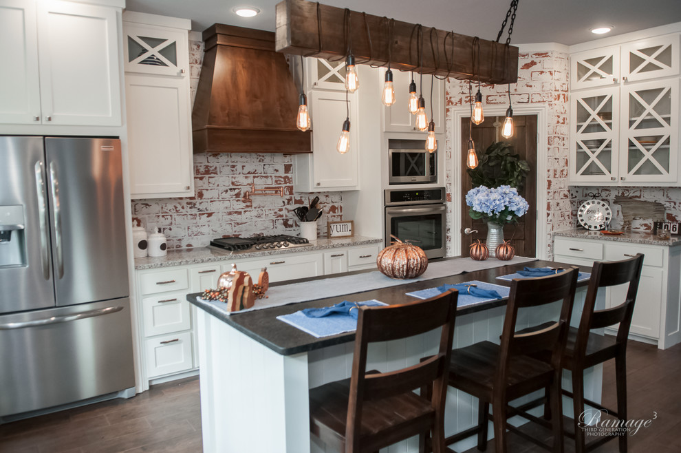 Example of a large transitional u-shaped brown floor open concept kitchen design with a farmhouse sink, shaker cabinets, white cabinets, granite countertops, multicolored backsplash, brick backsplash, stainless steel appliances, an island and gray countertops