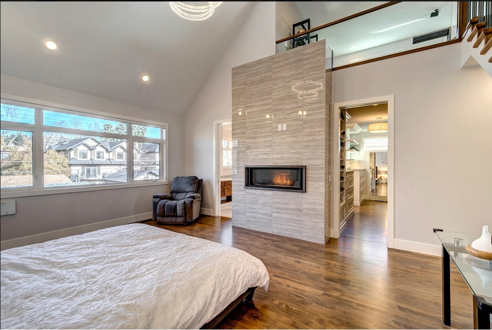 This is an example of a large traditional master bedroom in Calgary with a standard fireplace, a tiled fireplace surround and a vaulted ceiling.