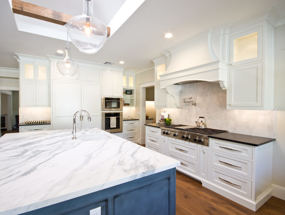 Inspiration for a large transitional u-shaped medium tone wood floor eat-in kitchen remodel in Phoenix with a farmhouse sink, recessed-panel cabinets, white cabinets, marble countertops, white backsplash, stone tile backsplash, stainless steel appliances and an island