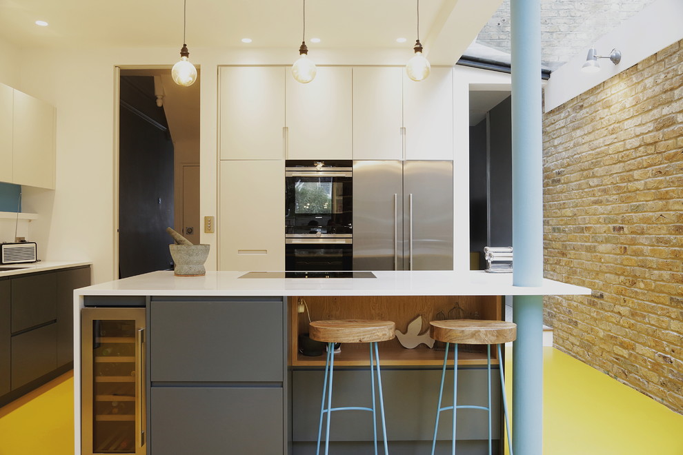 Inspiration for a large contemporary l-shaped eat-in kitchen in London with an undermount sink, flat-panel cabinets, grey cabinets, solid surface benchtops, white splashback, stainless steel appliances, with island, yellow floor and white benchtop.