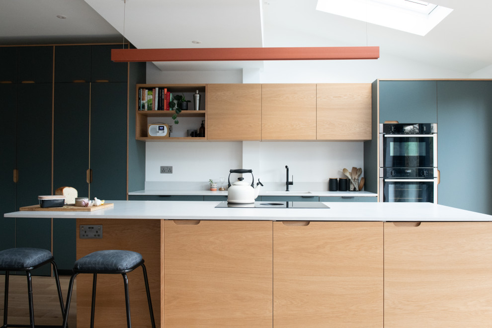 Design ideas for a scandinavian kitchen in London with an undermount sink, flat-panel cabinets, light wood cabinets, black appliances, with island, white benchtop and vaulted.