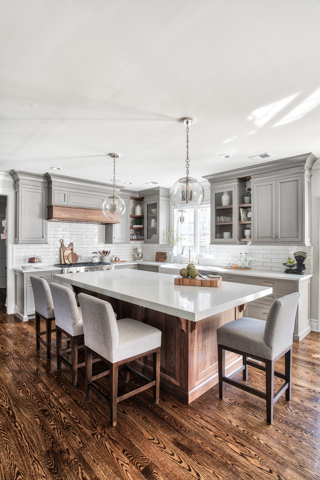 Kitchen pantry - mid-sized transitional u-shaped medium tone wood floor and brown floor kitchen pantry idea with a farmhouse sink, beaded inset cabinets, gray cabinets, solid surface countertops, gray backsplash, subway tile backsplash, stainless steel appliances, an island and white countertops