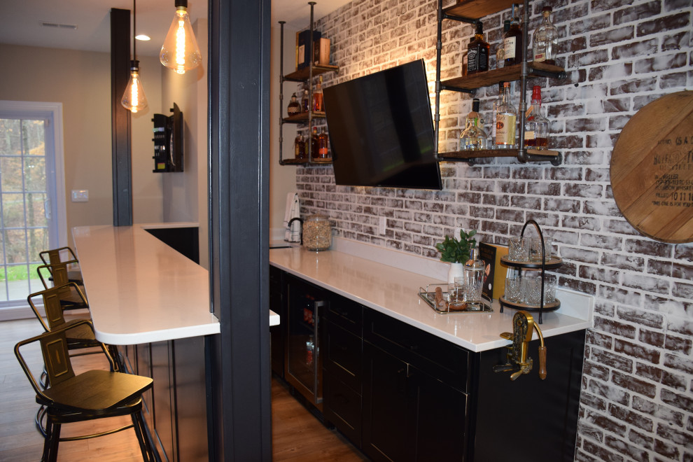 This is an example of a large industrial galley wet bar in Other with an undermount sink, shaker cabinets, black cabinets, quartzite benchtops, red splashback, brick splashback, light hardwood floors, brown floor and white benchtop.