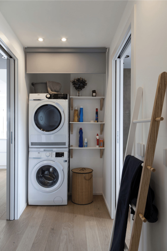 Small contemporary single-wall utility room in Other with white cabinets, white walls, light hardwood floors and a stacked washer and dryer.